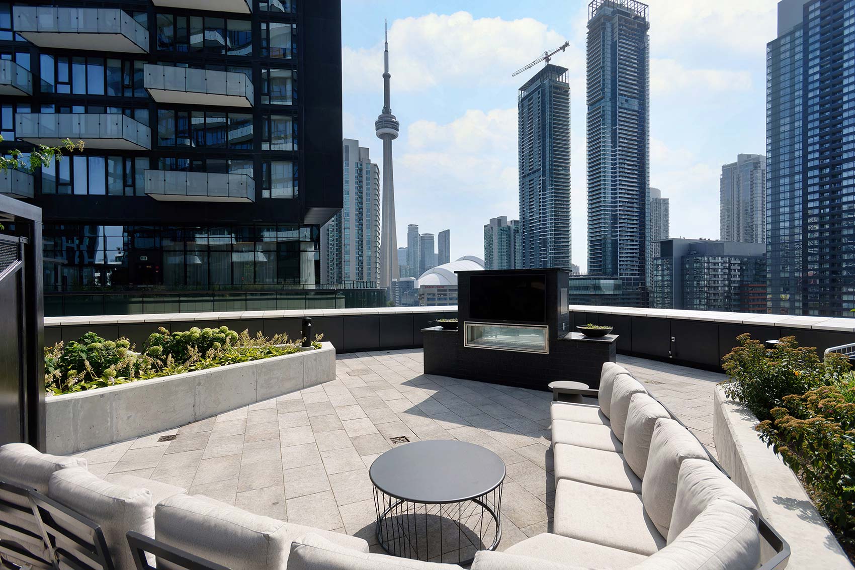 Furnished Condominiums Toronto: Rooftop terrace at The Well featuring a modern outdoor fireplace, large sectional sofa, and panoramic skyline views of the CN Tower.