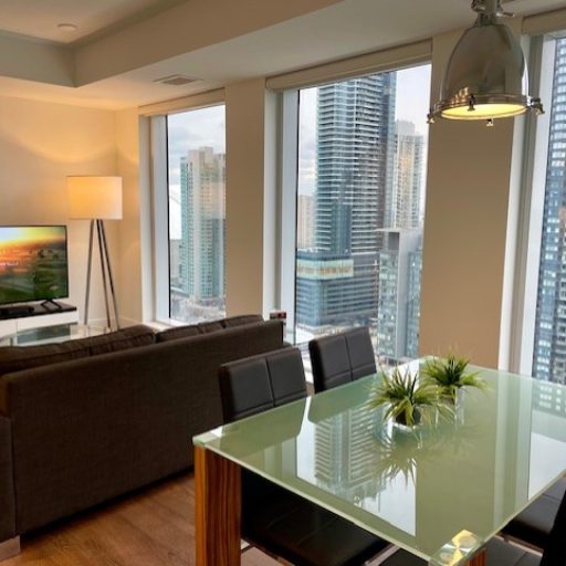Luxury Furnished Condominiums Toronto: Panoramic view of an executive open-concept living and dining area at The Well, featuring floor-to-ceiling windows with expansive city views.