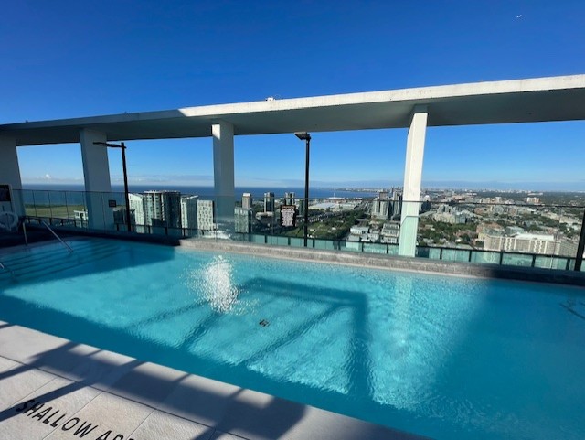 Luxury rooftop infinity pool at The Well featuring glass railings, white architectural pillars, and expansive southern views of the Toronto waterfront and Lake Ontario.